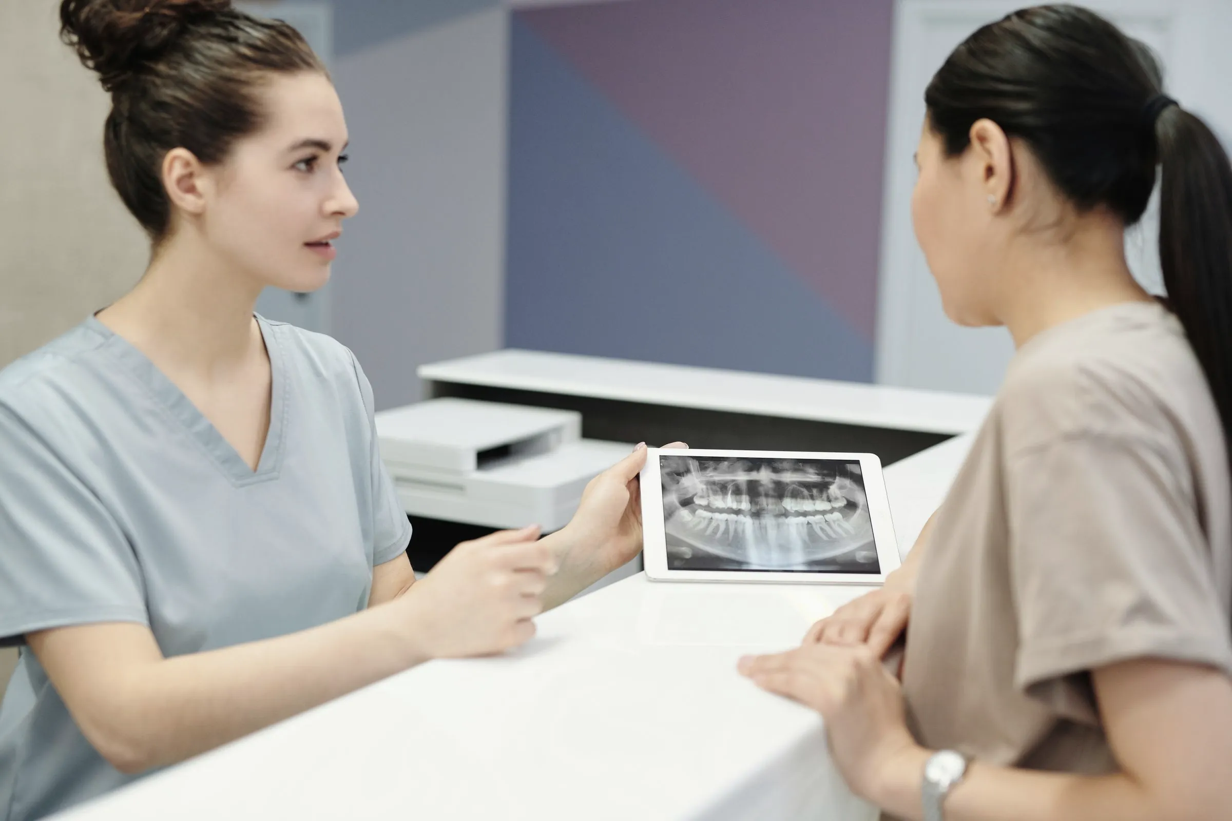 Auxiliar dental mostrando una radiografía panorámica a una paciente en la recepción de la clínica